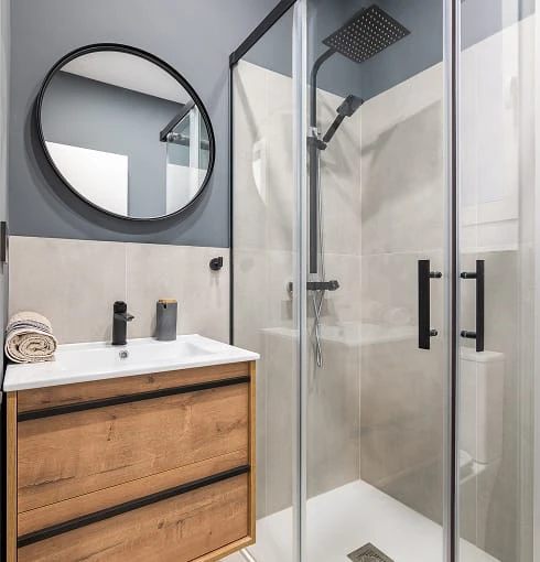 Salle de bain moderne avec douche vitrée, miroir rond et meuble-lavabo en bois