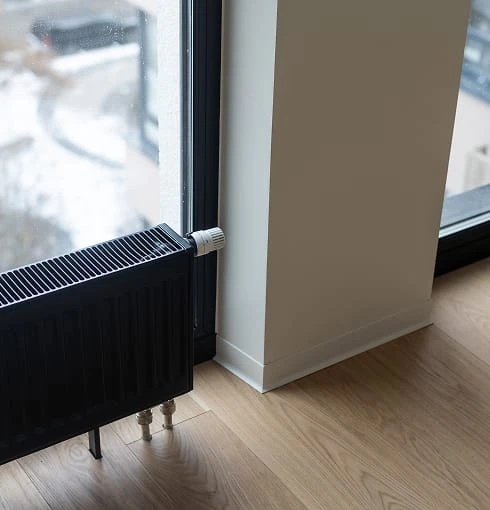 Radiateur noir moderne installé près d'une fenêtre dans une pièce avec parquet clair